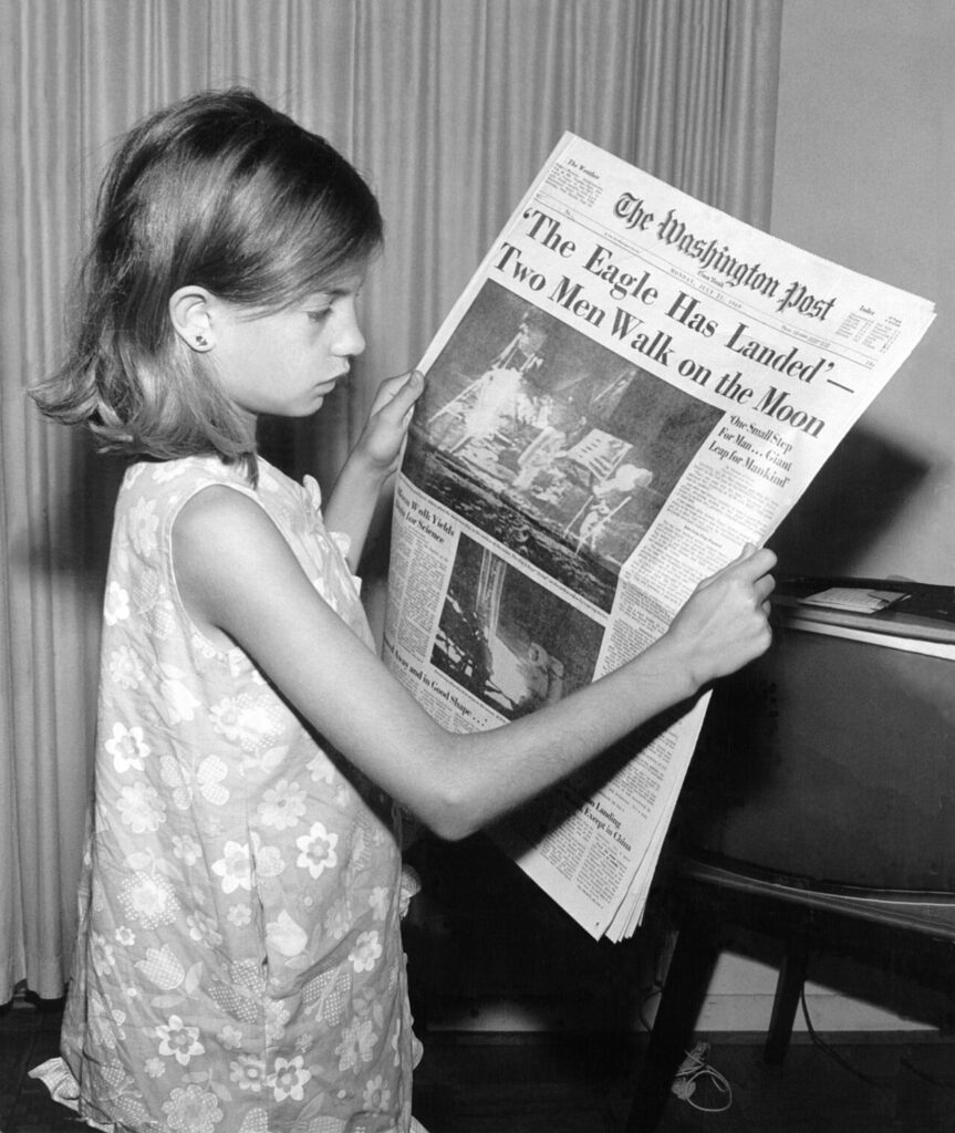 Fotografía histórica de una niña leyendo un periódico sobre la llegada a la Luna; ilustra la lectura de titulares, no una noticia falsa.